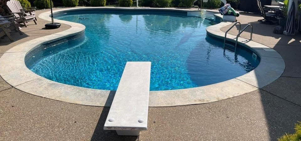 Swimming pool with lounge chairs, umbrella, and house in the background